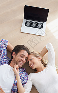 一个快乐的年轻夫妇在使用笔记本电脑后 躺在起居室的地板上 然后躺在地上 (笑声)图片