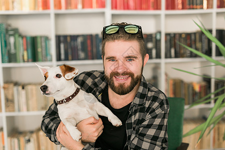 杰克罗素梗犬的快乐男主人 站在书架背景下 感到有责任照顾宠物 人与动物的关系感情男性成人晴天猎犬女性小狗朋友公寓犬类图片