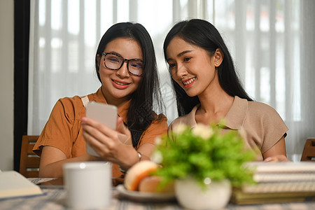 两名快乐的亚洲女学生在阅读书和检查手机社交媒体后休息 她们感到开心图片