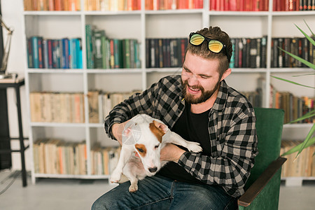 杰克罗素梗犬的快乐男主人 站在书架背景下 感到有责任照顾宠物 人与动物的关系犬类友谊成人小狗朋友情绪化感情猎犬男性公寓图片