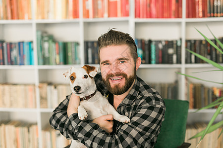 杰克罗素梗犬的快乐男主人 站在书架背景下 感到有责任照顾宠物 人与动物的关系晴天男性感情公寓朋友成人猎犬犬类友谊小狗图片
