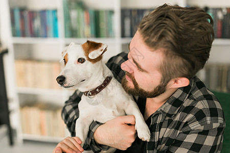 杰克罗素梗犬的快乐男主人 站在书架背景下 感到有责任照顾宠物 人与动物的关系小狗犬类猎犬情绪化感情友谊成人男性晴天朋友图片