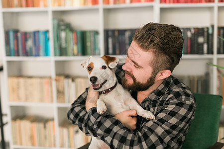 杰克罗素梗犬的快乐男主人 站在书架背景下 感到有责任照顾宠物 人与动物的关系朋友男性晴天小狗成人犬类女性友谊公寓猎犬图片