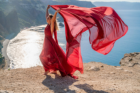 一个穿着红色飞行服的女人 在大海的背景下 飘在风中发抖着成人幸福女孩尾巴太阳海洋衣服天空丝绸日落图片