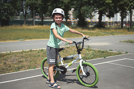 活跃的高加索男孩 穿着运动头盔 看着摄像机 站在户外沥青路上的自行车旁 (笑声)图片