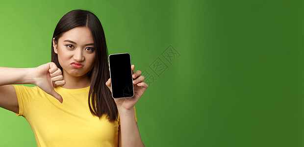 特写失望心烦意乱的亚洲女孩判断糟糕的糟糕应用程序 显示智能手机屏幕 拇指向下的鬼脸不高兴 给出负面反馈 无法忍受前男友的新女友情图片