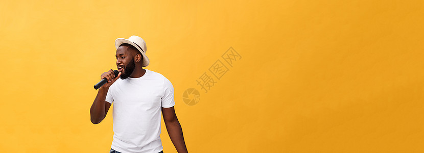 年轻英俊的非裔美国男孩唱着情感歌曲 用麦克风孤立在黄色背景上 在运动中游荡音乐家卡拉ok娱乐男生快乐唱歌成人音乐会居住男性图片