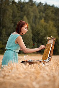 专业画家女孩 在成熟小麦田从事绘画工作图片