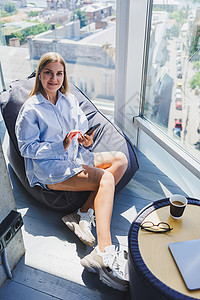 一名年轻女子坐在扶手椅上 用手机用耳机听音乐 工作一天后 漂亮女人在带大窗户的联合办公空间放松身心列表闲暇沙发房子女性享受技术长图片