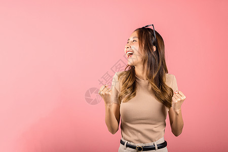 年轻女青年戴眼镜 举起手来庆祝她成功胜利的姿势青少年手势学生快乐优胜者欢呼女孩拳头乐趣微笑图片