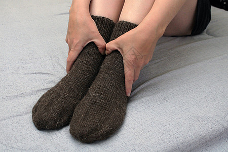 一位长着苗条双腿的年轻女子穿着棕色羊毛袜坐在家里的床上 世界能源危机的概念衣服加热袜子羊毛房间房子床单织物气体短袜图片