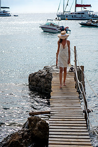 穿着帽子和轻面衣的白发女人 在海边行走海滩裙子闲暇假期码头白色蓝色太阳天空海洋图片