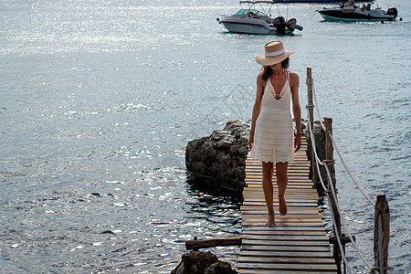 穿着帽子和轻面衣的白发女人 在海边行走太阳海滩天空蓝色女孩美丽闲暇假期裙子海洋图片