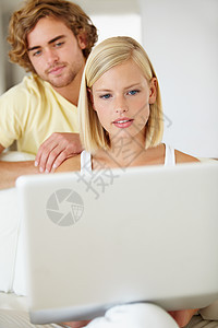 一起使用笔记本电脑 一位美丽的年轻女子正在浏览笔记本电脑 而她的男友则在她身后观看图片