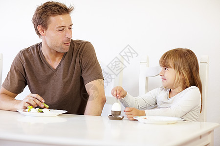 一个小女孩坐在桌子上 和她爸爸一起吃早饭 然后和父亲共进晚餐图片