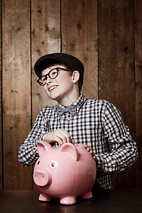 每分钱都存着 穿旧装的年轻男孩把钱放进他的小猪库图片