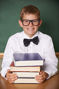 他为考试做准备 一个快乐的年轻男学生戴着眼镜 在照相机上笑着领带 坐在一叠书本旁图片