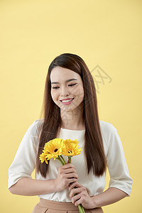穿着白衬衫的漂亮女人 手里拿着黄色背景的鲜花 她微笑着大笑女孩女性花朵金发女郎花束成人礼物白色雏菊图片