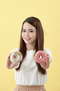 年轻美丽的亚洲妇女穿着白色T恤衫 微笑和欢乐 带着甜甜圈 孤立在黄色背景上蛋糕粉色乐趣女性舌头女士甜点饮食食物图片