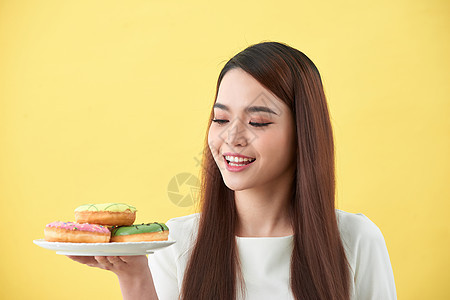 美丽的年轻女人微笑着拿着一盘装满美味彩色甜甜圈的盘子成人食物白色小吃垃圾女孩女性甜点饮食图片
