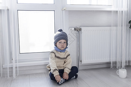 穿毛衣的小孩和灰帽 跪在加热器旁边 用自动调温器图片