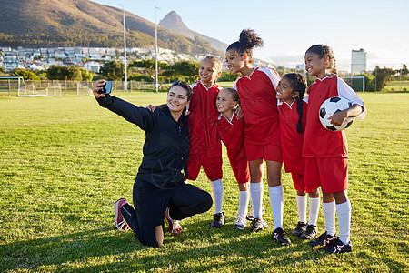在体育俱乐部训练 练习或比赛后 足球 球队和教练用手机在球场上自拍 足球女子团体在运动场上为社交媒体合影时微笑和开心图片
