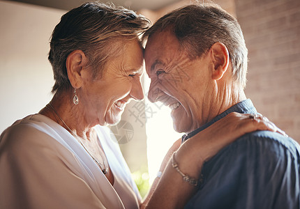 男女拥抱爱 快乐和笑的老年夫妇在家里拥抱和联系在一起 开朗地分享一个有趣的笑话 享受退休和嬉戏乐趣的老年男女的幽默 关怀和感情背景
