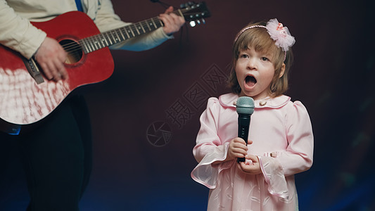 穿旧礼服的小女孩在舞台上唱歌 她父亲弹声吉他戏服爱好才俊爸爸连衣裙衣服幼儿园国家舞蹈岩石图片