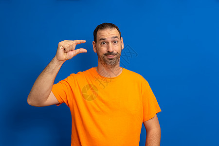 西班牙裔男子站在蓝色背景上 带着怀疑的面孔用手摆动 用手指看和相机做小标志图片