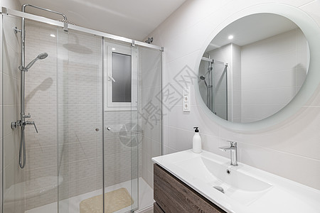 白色瓷砖洗手间 墙上长着大圆镜 用玻璃栏杆和金属配件反映淋浴区图片