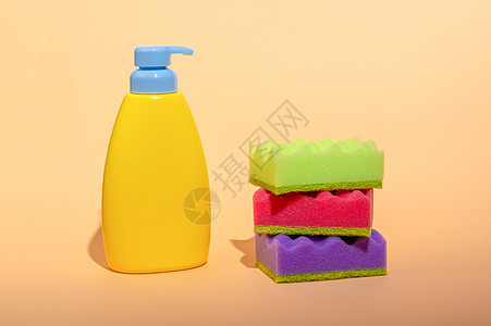 堆叠着多色洗碗海绵 在面橙背景上装满肥皂瓶 家庭清洁清洗板 家庭清洁概念图片