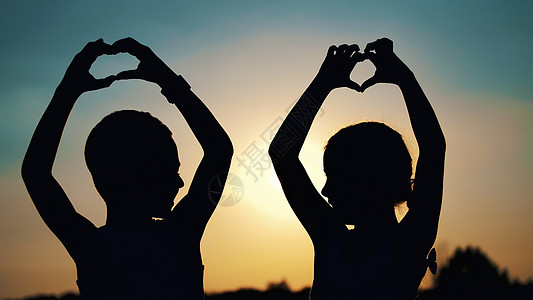 夏季日落时分 儿童 男孩和女孩的剪影 人物形象在太阳的背景下用手指 手展示心灵 幸福的家庭 慢动作成人男人男生女性街道拥抱孩子乐图片