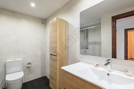 现代洗手间有白色瓦岩墙 小型的卫生用木箱和毛巾坐在墙上 颜色与水槽的橱柜相协调 镜子反射门进入房间图片