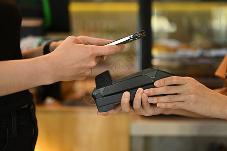 女性客户持有手机和扫描qr码 在咖啡店支付无接触移动电话费的裁剪镜头图片