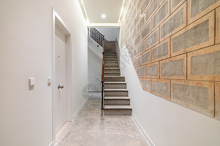 带木栏杆的石楼梯通向明亮走廊中的二楼 浅色现代时尚走廊 白色门 灰色砖墙上装饰 每间都采用浅棕色框架图片
