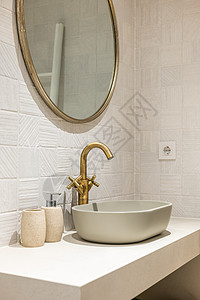 现代浴室的白色光滑大理石台面上的椭圆形时尚水槽 古铜色的双阀水龙头与挂在墙上的圆镜和房间内的其他物件相得益彰图片