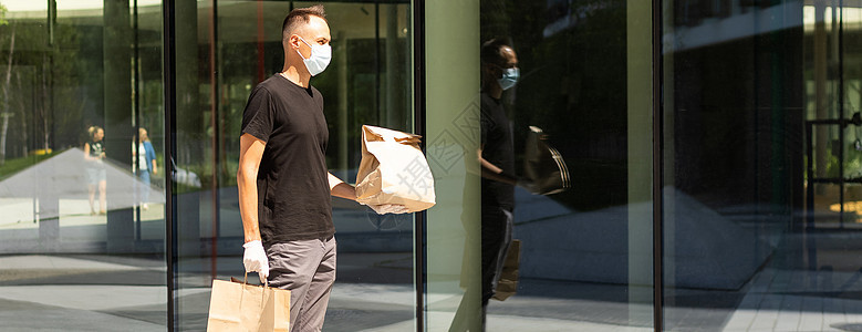 带保护面罩和手套的送货员拿着包 在大楼前面有杂货危害志愿者男性健康送货疾病房子流感生物购物图片