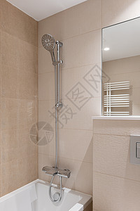 带浴缸的浴室一角 俯瞰带大圆形淋浴头的不锈钢金属水龙头 墙上是镜子的一小部分 反射出用于晾干毛巾的白色散热器的一部分图片