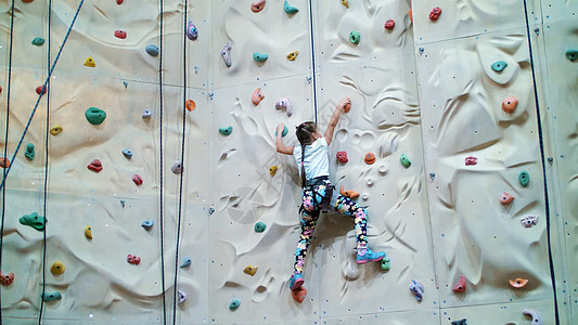 孩子爬上登山专用墙 安全设备七年的女孩在特训垂直墙上从事攀岩娱乐冒险首脑绳索力量登山者学习操场行动风险图片
