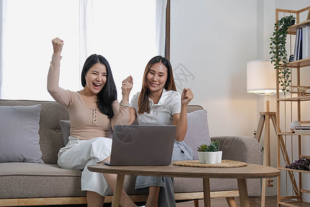 两个快乐的亚洲女性最好的朋友在客厅用笔记本电脑在家工作时 穿着随意穿着笑装房子购物女孩微笑房间青少年团体姐姐长椅沙发图片