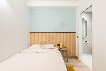 双人床靠着一个浅壁龛 墙壁是蓝色的 装饰有木制装饰 在卧室里 有一扇敞开的门可以俯瞰明亮的卫生间 里面有马桶和一个小塑料窗家具入图片
