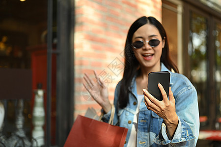 站在城市购物区自拍或用手机打视频电话的快乐亚洲女性图片