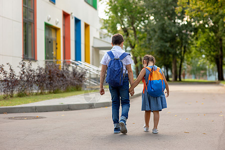 两个学童 一个小女孩和一个男孩背着背包走在上学的路上领带运动孩子书包兄弟蓝色学校自由微笑日落图片