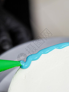手工糕点厨师设计师 将一个霜冻的白蛋糕涂上浅蓝色淡面粉滴装充袋烹饪美食家管道职业磨砂商业美食诱惑奶油滴水图片
