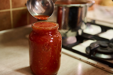 选择性地关注一个绝育罐头罐头和家庭主妇 从酱盆里倒新鲜酿造的番茄汁图片