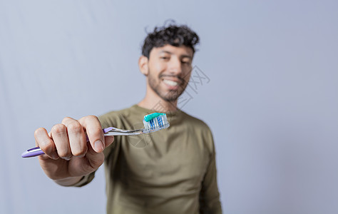 尼加拉瓜微笑的男人在前景中展示一把牙刷 显示有牙膏的微笑的年轻人牙刷被隔绝 微笑的人拿着带牙膏的牙刷和复制空间背景