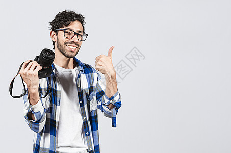 微笑的男摄影师展示相机并竖起大拇指 年轻人拿着相机竖起大拇指 微笑的男摄影师用大拇指展示相机图片