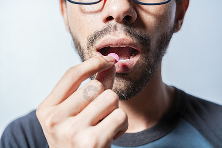 服用药丸的人被隔离 年轻人把药丸放在嘴里的特写镜头 自我药疗概念 男人在嘴里放一颗药丸 一个男人服用阿司匹林的特写镜头图片