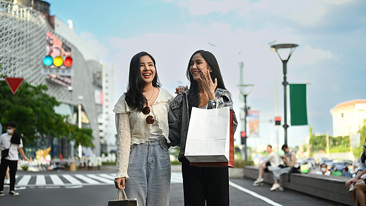 时装女性朋友和购物袋的朋友站在城市街道上 背景是城市风景模糊 天空蓝淡的背景图片