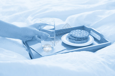 女性手在托盘上举着水杯 床上装着饼干营养食物玻璃早餐节食蓝色饮食白色桌子图片